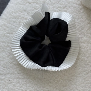 Detailed view of black satin scrunchie with elegant white pleated ruffled edge trim