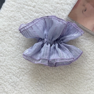 Close-up of purple organza scrunchie with layered ruffle edges on soft white texture