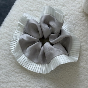 Detail of silver grey satin scrunchie with white pleated lace on soft plush background