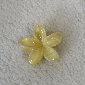 Pince à cheveux fleur de frangipanier avec texture marbrée jaune sur fond en peluche