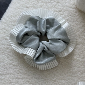 Detail of grey satin scrunchie with white pleated lace trim on a soft textured background