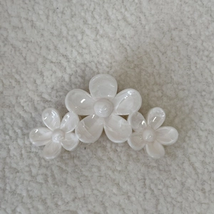 Détail de la pince à cheveux à trois fleurs avec fini nacré sur fond texturé blanc cassé