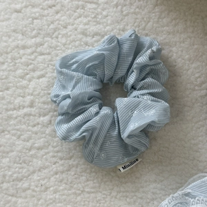 Detail of light blue striped scrunchie with floral embroidery and brand label