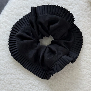 Detailed view of the pleated black silk satin fabric on a large scrunchie accessory
