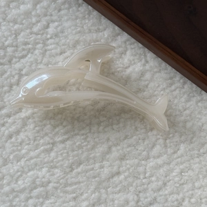 Détail de la pince à cheveux dauphin blanc nacré sur fond de tissu doux texturé
