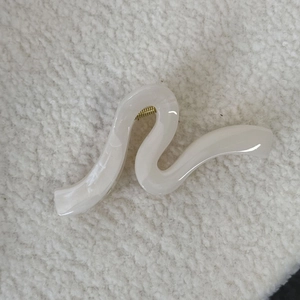 Détail macro d'une pince à cheveux ondulée blanc crème brillant avec ressort doré