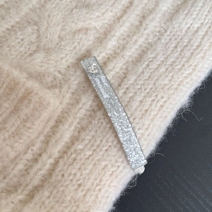 Dettaglio di un fermaglio per capelli argento glitterato con cuore su maglia beige
