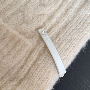 Dettaglio di un fermaglio bianco rettangolare con cristallo a cuore su un maglione di maglia