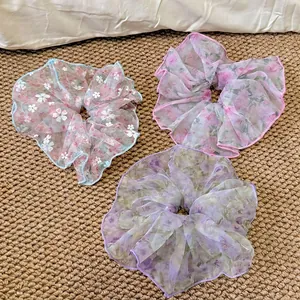 Lot de trois chouchous à fleurs en maille bleu, rose et violet sur un tapis tissé