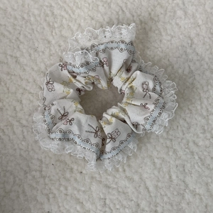 Detailed close-up of floral scrunchie with pink bows and white lace trim on plush background