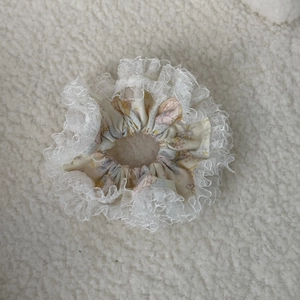 Detailed view of floral scrunchie with layered white lace edges on soft white background