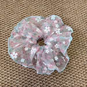 Détail d'un chouchou en organza rose avec bords volantés bleu clair et motif floral