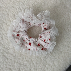 Close-up of white floral lace scrunchie with red heart patterns on soft fabric