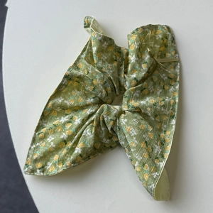 Macro detail of green floral fabric scrunchie with rabbit ear bow and soft pleats