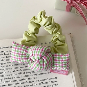 Zoete haarelastiek met geruite strik en Tuesday-label op een boek voor haaraccessoires