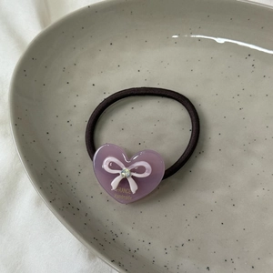 Détail d'un élastique à cheveux en acétate avec cœur, nœud, strass et logo doré