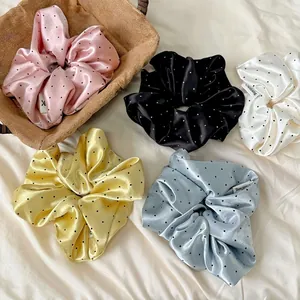 Five assorted colors of silky polka dot scrunchies set on soft fabric background