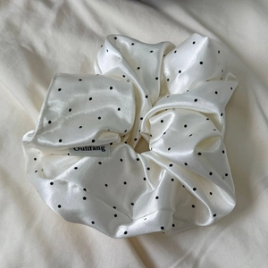 Close-up of a white satin polka dot scrunchie featuring a minimalist logo cloth tag