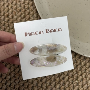 Detail showing two marble textured oval hair clips on a white brand display card