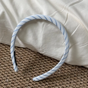 Close-up of a slim blue and white striped fabric headband with a brand label detail