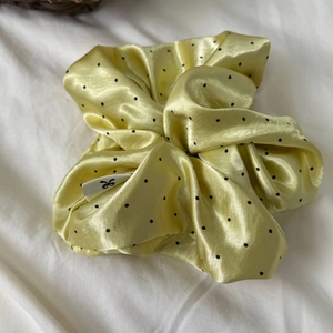 Polka dot yellow satin scrunchie with subtle brand logo on textured fabric background
