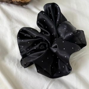 Detail shot of a black satin scrunchie with white polka dots on soft fabric background