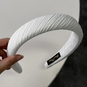 Close-up of a white pleated sponge headband showing fine fabric texture and brand label