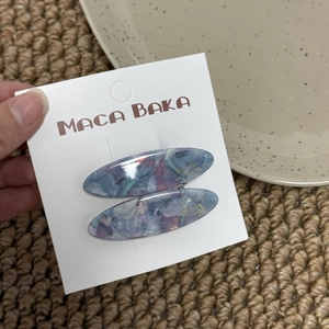 Detail showing two blue marble acetate willow leaf hair clips on a brand display card