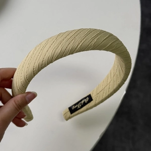 Close-up of pleated beige fabric headband showing thick sponge texture and handmade label