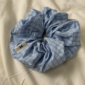Light blue and white plaid fabric scrunchie with soft cotton texture and woven label