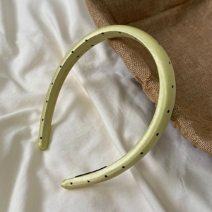 Close-up of a padded lime green satin headband with black polka dots on white fabric