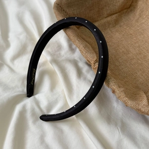 Detailed shot of a black polka dot headband featuring glossy satin fabric and gold logo