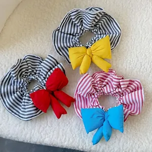 Three colorful bow hair scrunchies with stripes on a white plush background