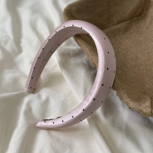 Close-up of pink satin headband with black polka dots on white draped fabric