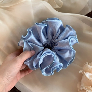 Detailed close-up of light blue satin scrunchie with layered ruffle edges and silk texture