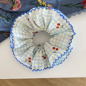 Gros plan d'un chouchou à carreaux bleu et jaune avec broderie cerise et dentelle