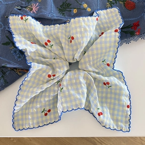 Détail de chouchou à carreaux avec broderie cerise et bords ondulés bleus