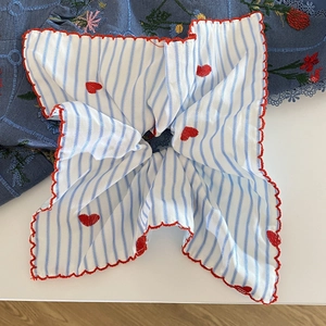 Gros plan d'un tissu à rayures bleues avec broderie de cœurs rouges et bord festonné