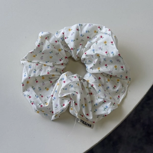 Close-up of white floral scrunchie with colorful prints and branded woven label detail