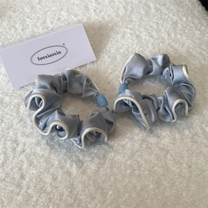 Detail of two light blue satin scrunchies with white piping and bead accents on soft rug