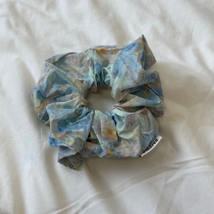 Detailed view of a light blue floral scrunchie with a soft fabric texture and logo label