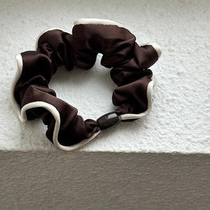 Detailed close-up of dark brown satin scrunchie with cream white piped edge and oval bead
