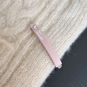 Dettaglio di un fermaglio per capelli rosa con strass a cuore e testo su sfondo in maglia