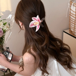 Detail of a pink magnolia flower hair clip with translucent ribbon on long wavy hair
