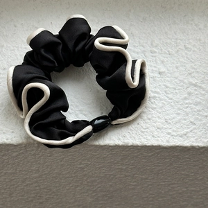 Detailed close-up of a French style black satin scrunchie with cream white piping edge