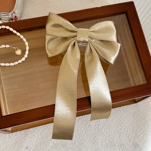 Detailed view of champagne gold metallic fabric bow hair clip with long ribbons