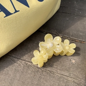 Détail macro d'une pince à cheveux florale jaune crème avec texture marbrée sur bois