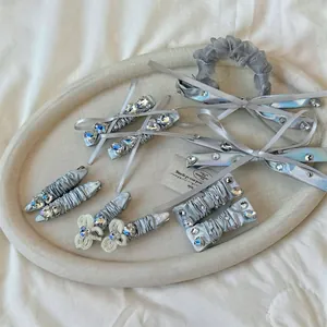 Silver PU leather bow hair clip and rhinestone scrunchie set on a beige display tray