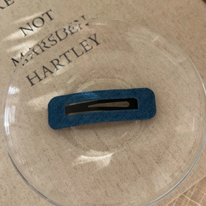 Detailed view of rectangle denim hair clip with hollow metal center on linen background