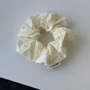 Creamy white oversized scrunchie with soft pleated texture and minimalist side label